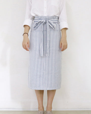 Person wearing a white shirt and striped apron against a plain background