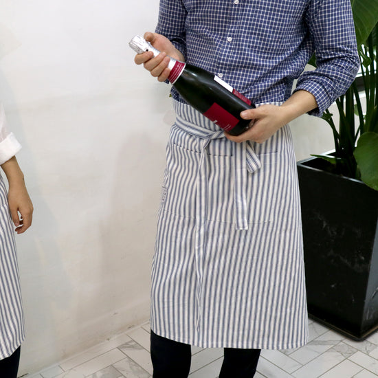Two people wearing striped aprons holding bottles in a room with a plant.