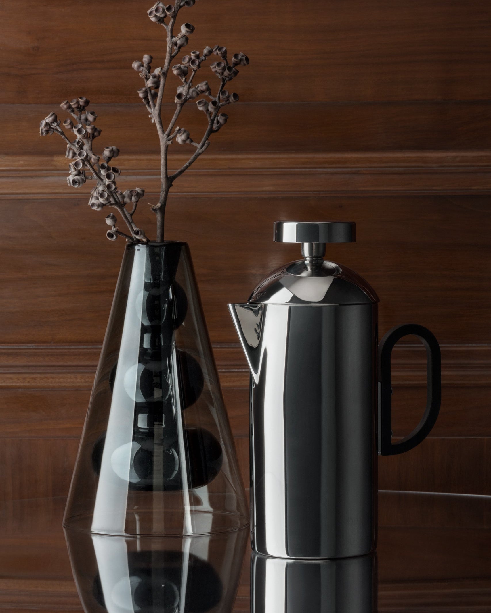 Silver brew cafetiere on a reflective surface with a wooden background
