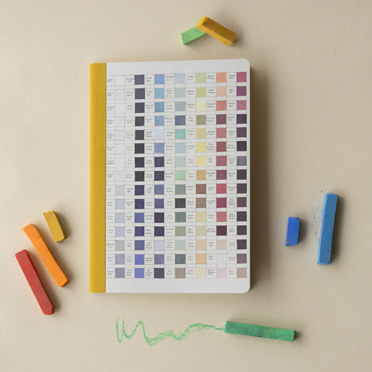 Notebook with color swatch pages surrounded by colorful crayons on a beige background