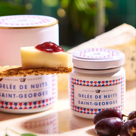 Two jars of 'Gelée de Nuits Saint-Georges' with a slice of cake and jam on a wooden surface.