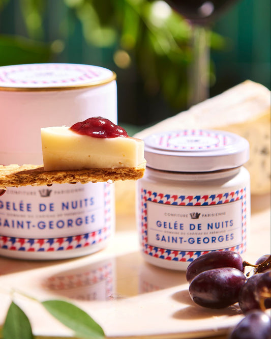 Two jars of 'Gelée de Nuits Saint-Georges' with a slice of cake and jam on a wooden surface.