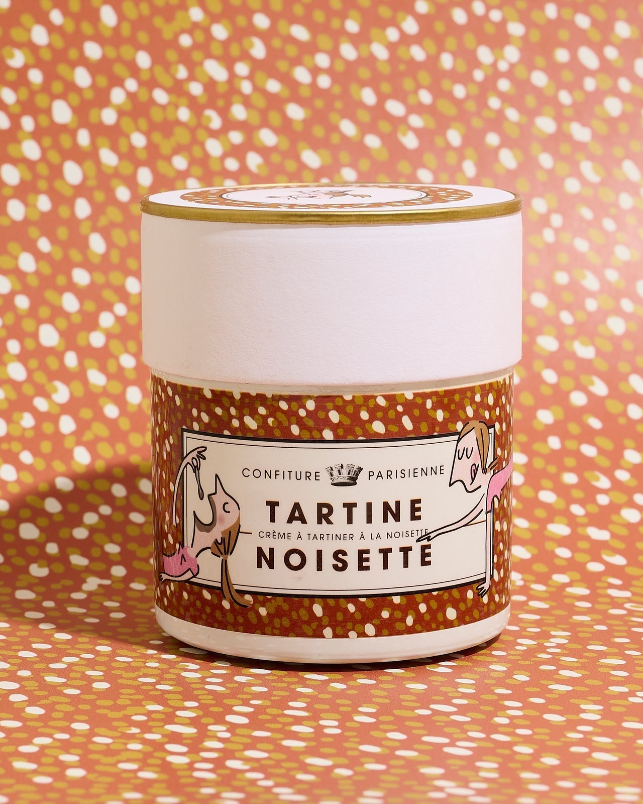 A jar of hazelnut spread with illustrated characters on the label, placed against a dotted orange patterned background