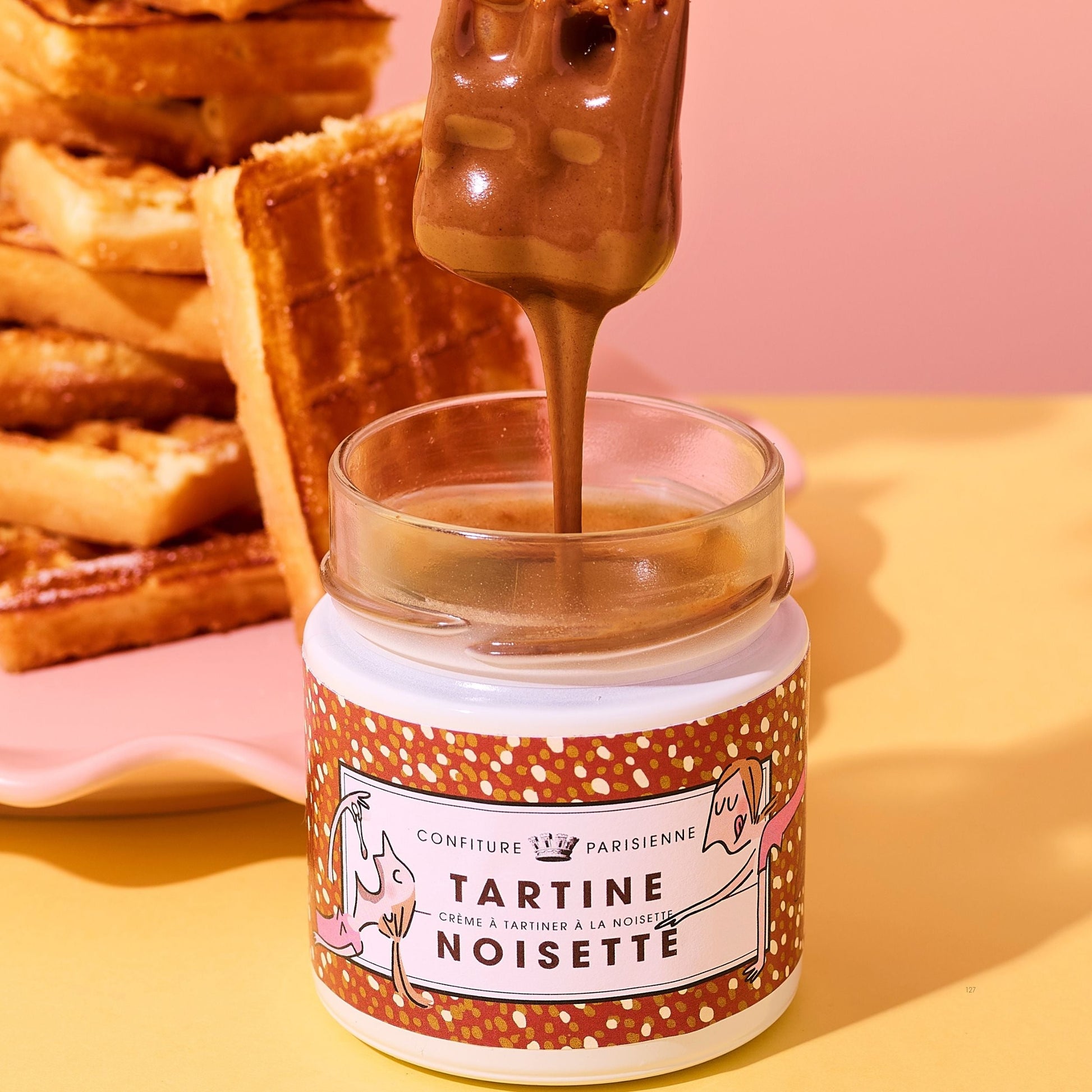 Jar of Tartine Noisette with a spoon pouring chocolate onto a pink background