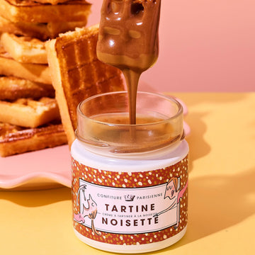Jar of Tartine Noisette with a spoon pouring chocolate onto a pink background
