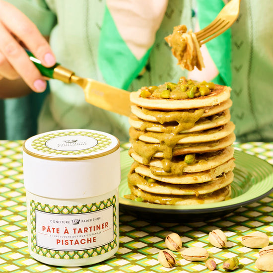 Stack of pancakes with pistachio butter on a green tablecloth, with a container of pistachio butter.