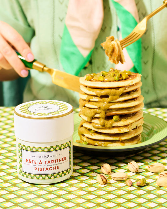Stack of pancakes with pistachio butter on a green tablecloth, with a container of pistachio butter.