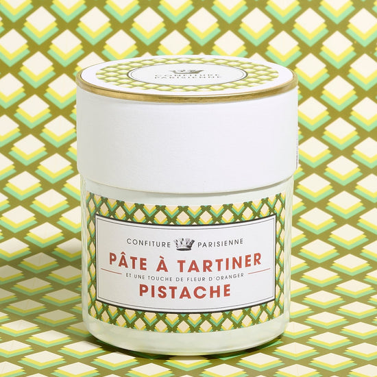A jar of pistachio spread with a green patterned label, placed against a matching geometric background