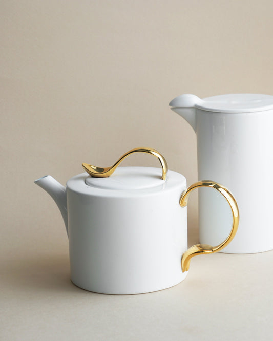 White ceramic teapot and milk jug with gold handles on a beige background