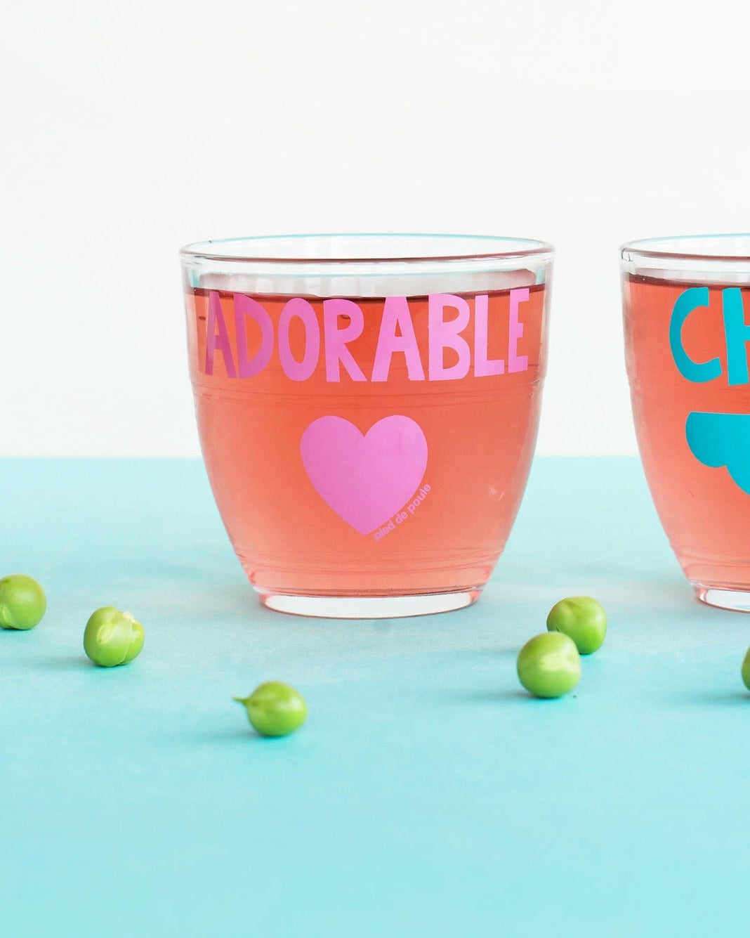 Two glasses with 'ADORABLE' and 'CHOU' text on a light blue background with green peas.