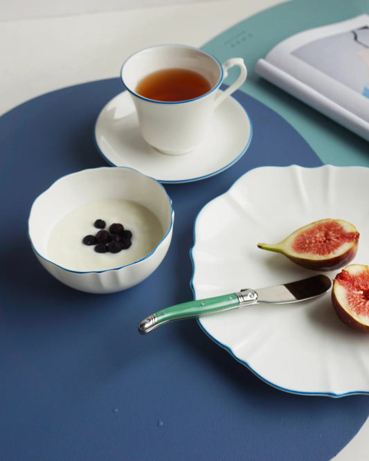 Teacup with tea, bowl of blackberries, and plate with figs on a blue placemat.