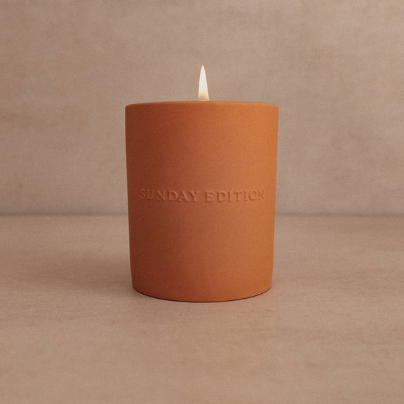 Terracotta-colored candle with 'Sunday Edition' branding on a beige background
