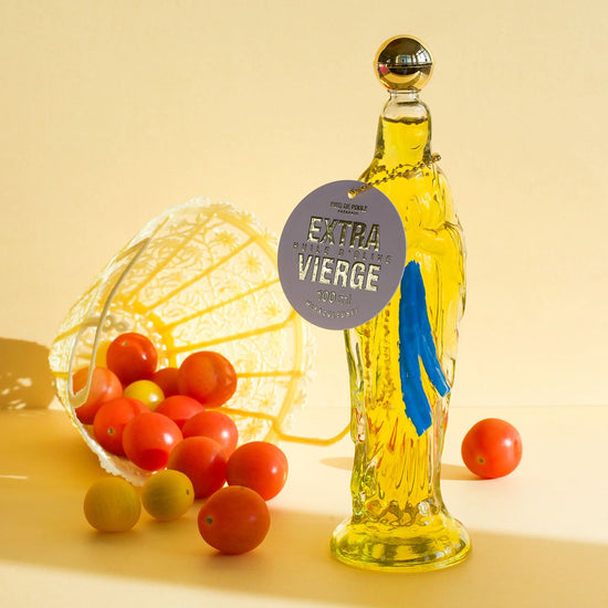 Bottle of Satura Vierge olive oil with a tag, surrounded by tomatoes on a yellow background