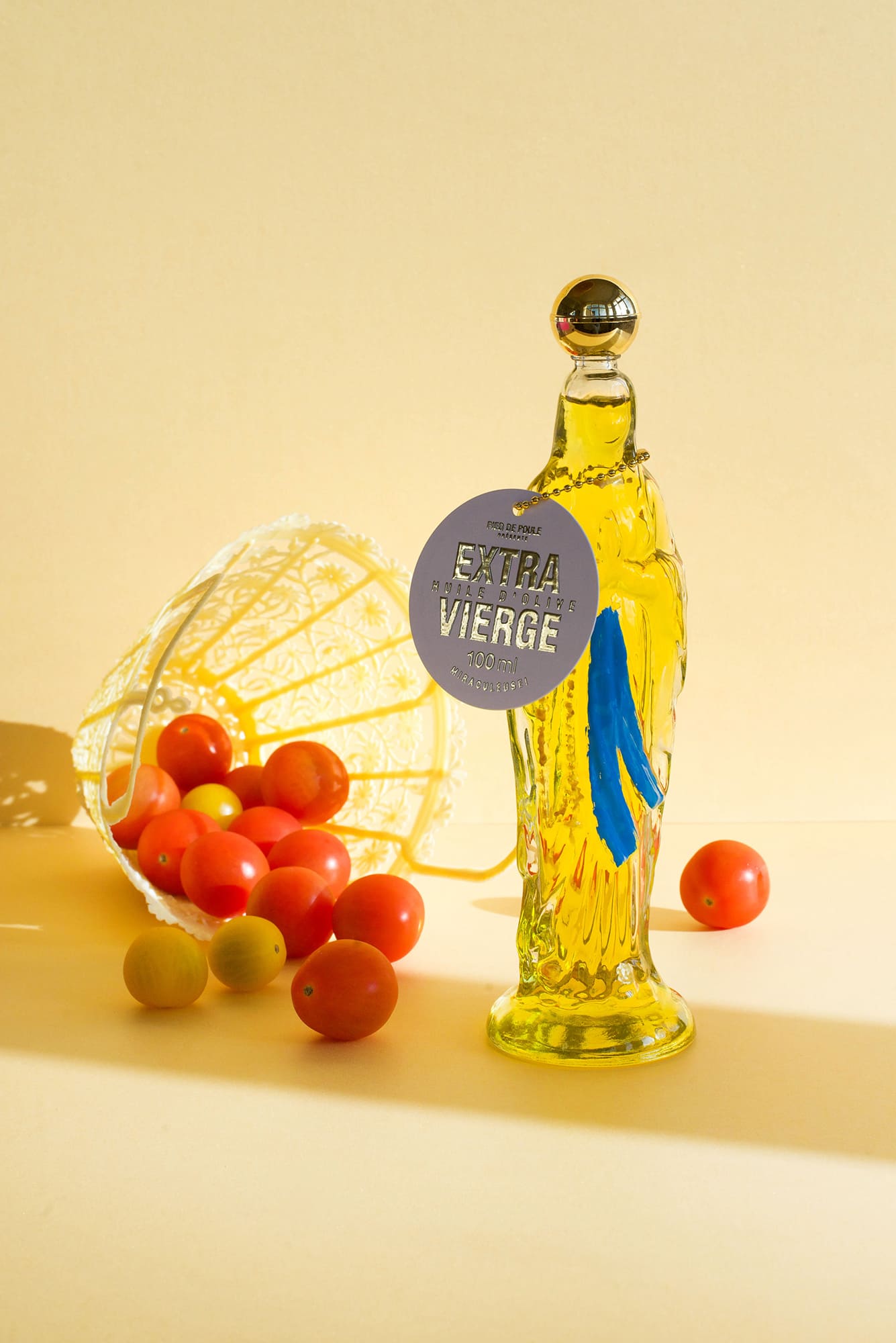 Bottle of Satura Vierge olive oil with a tag, surrounded by tomatoes on a yellow background