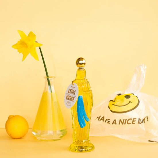 Yellow bottle with a smiley face label, lemon, vase with yellow flower, and 'Have a Nice Day' bag on a yellow background