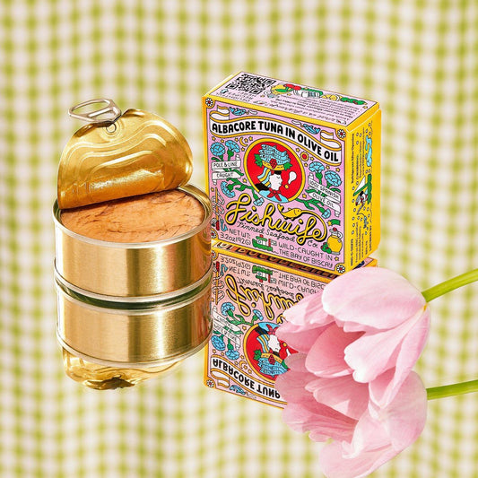 Tuna can with gold lid, colorful box, and pink flower on a green checkered background