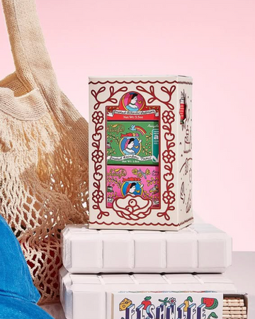 Blue cap, beige mesh bag, and boxes with colorful designs on a pink background