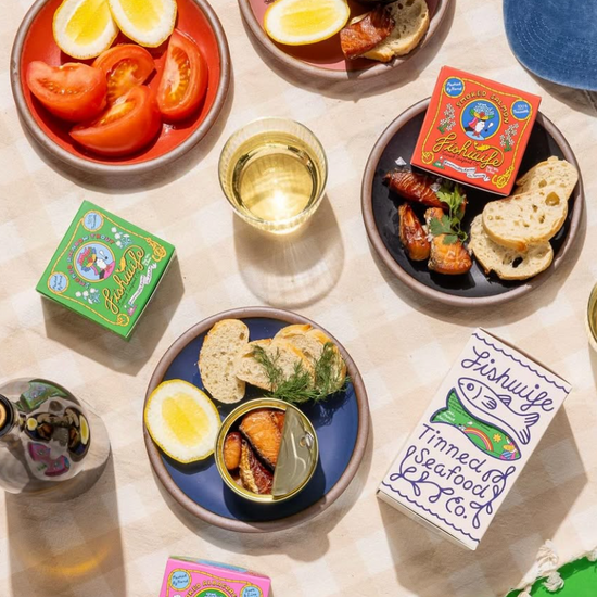 Table setting with fishwife tins, lemon wedges, and bread on a light surface.