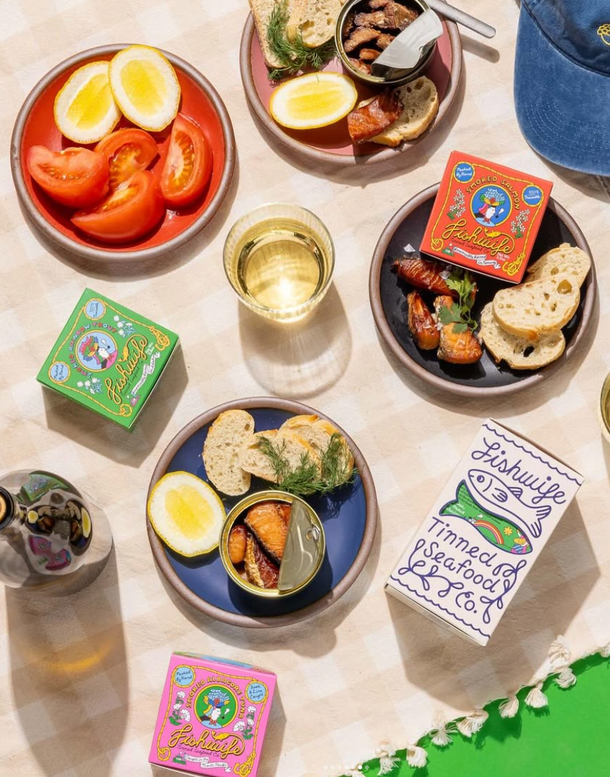 Table setting with fishwife tins, lemon wedges, and bread on a light surface.
