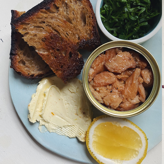 Plated meal with bread, mayonnaise, canned tuna, lemon, and greens on a light blue plate.