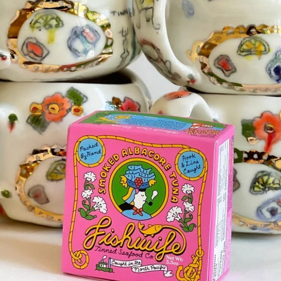 Pink 'Fishouta' tuna can box with decorative tea cups in the background