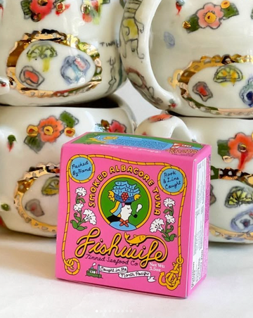 Pink 'Fishouta' tuna can box with decorative tea cups in the background