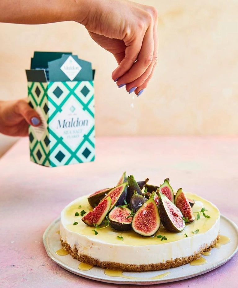 Cheesecake with figs on a plate next to a container of Maldon sea salt.
