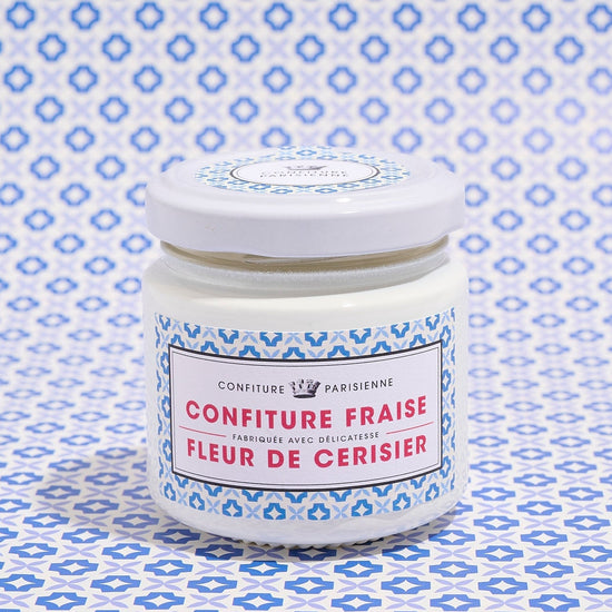 A jar of strawberry and cherry blossom jam with a blue patterned label against a matching patterned background