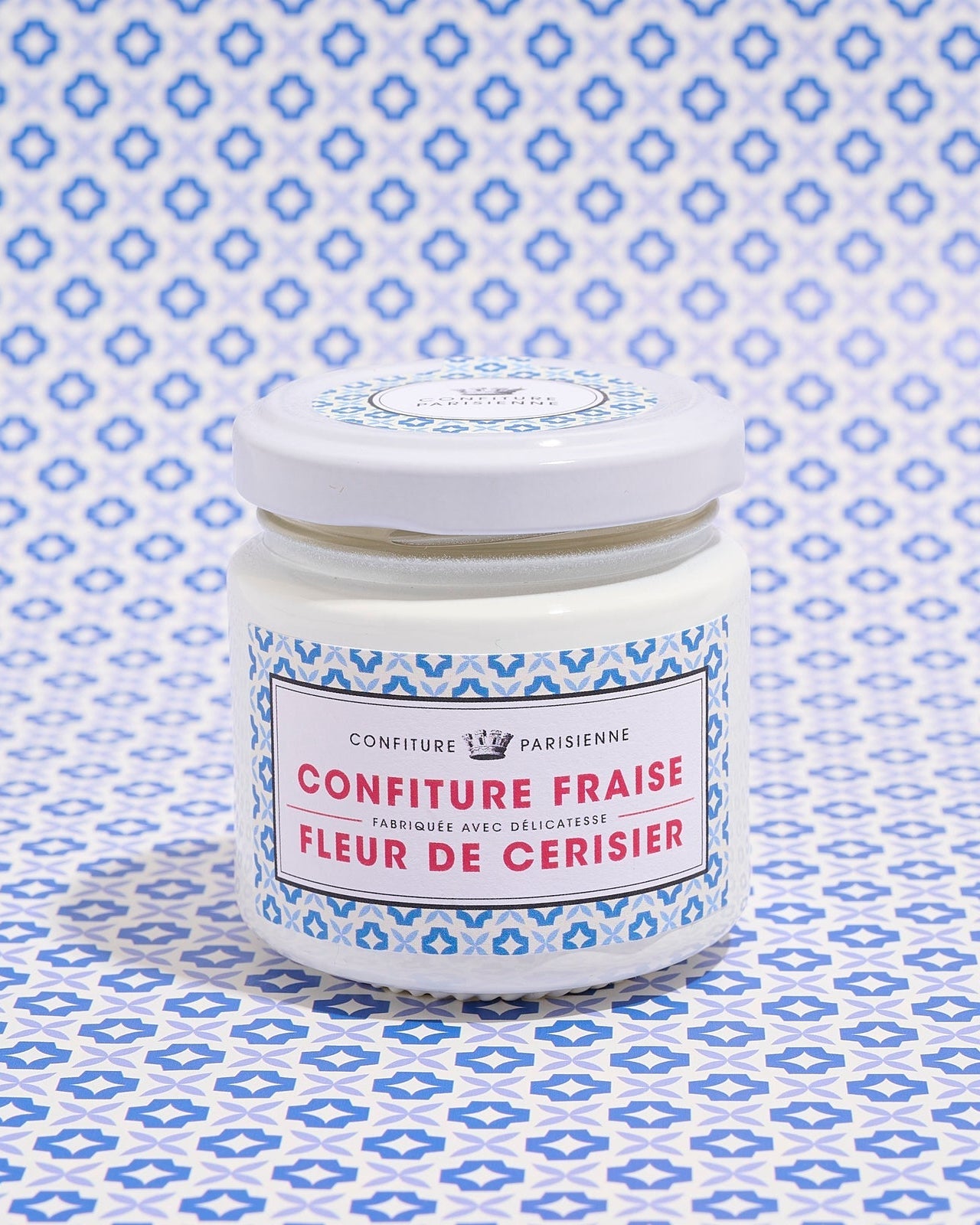 A jar of strawberry and cherry blossom jam with a blue patterned label against a matching patterned background
