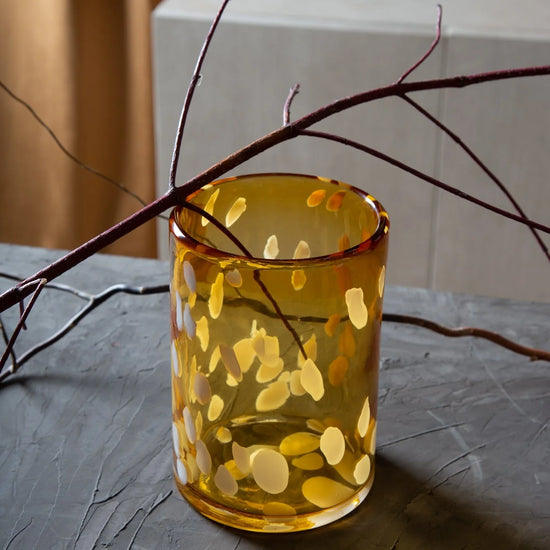Yellow glass with circular patterns on a textured surface with branches.