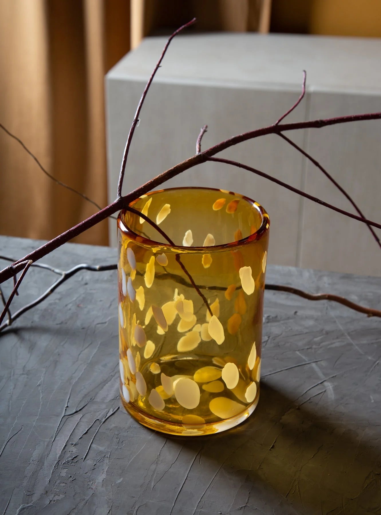 Yellow glass with circular patterns on a textured surface with branches.
