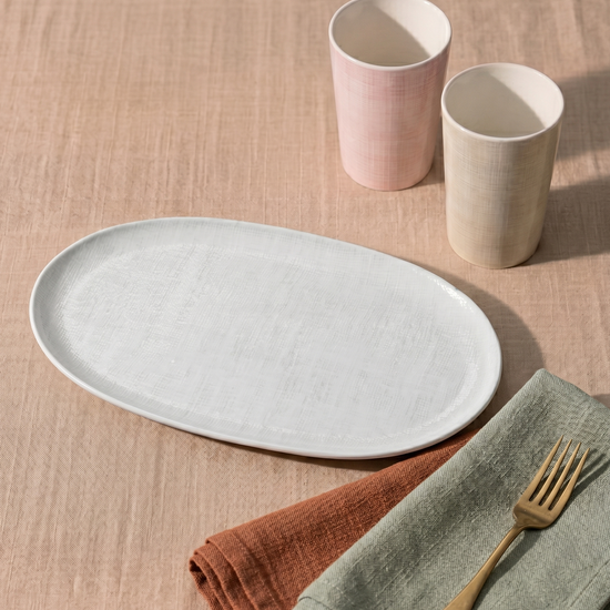 Table setting with a white plate, pink and beige cups, gold fork, and folded napkins on a beige tablecloth.