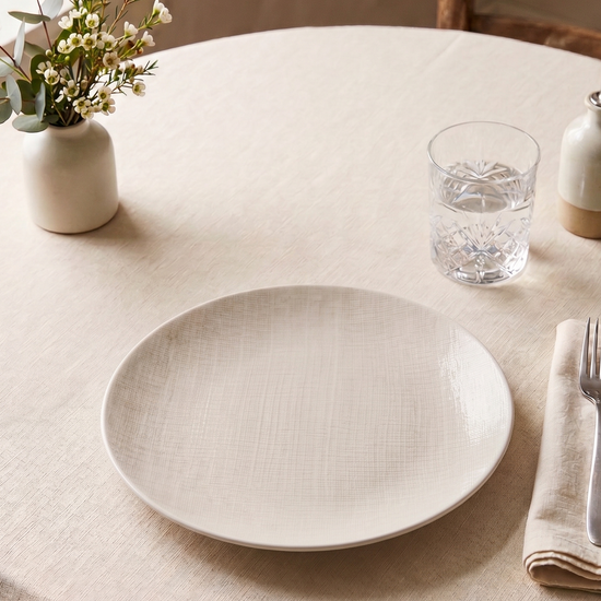 Round table setting with a white plate, cutlery, and decorative elements.
