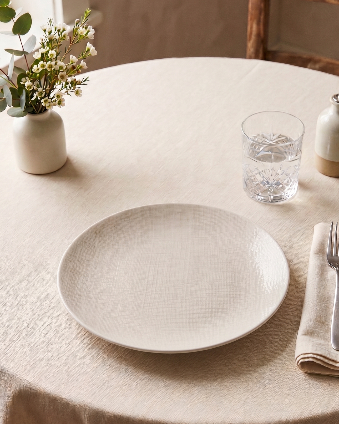 Round table setting with a white plate, cutlery, and decorative elements.