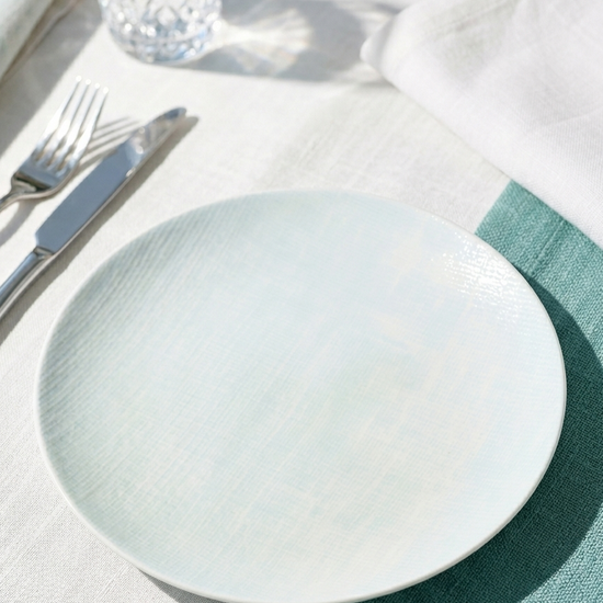Light blue plate on a white tablecloth with silverware and a glass.