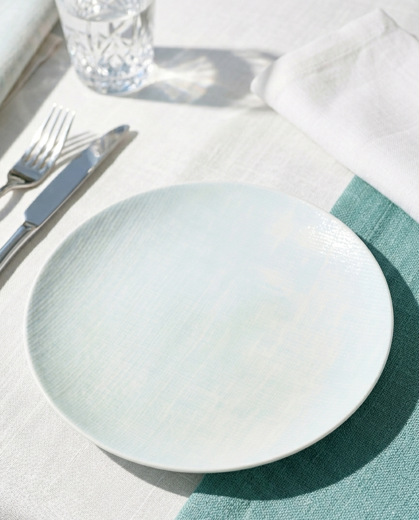 Light blue plate on a white tablecloth with silverware and a glass.