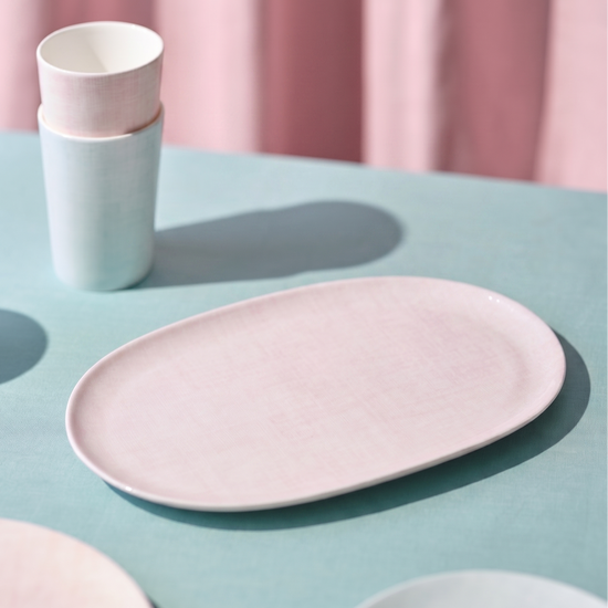 Pink ceramic plate and cups on a light blue surface with pink curtains in the background