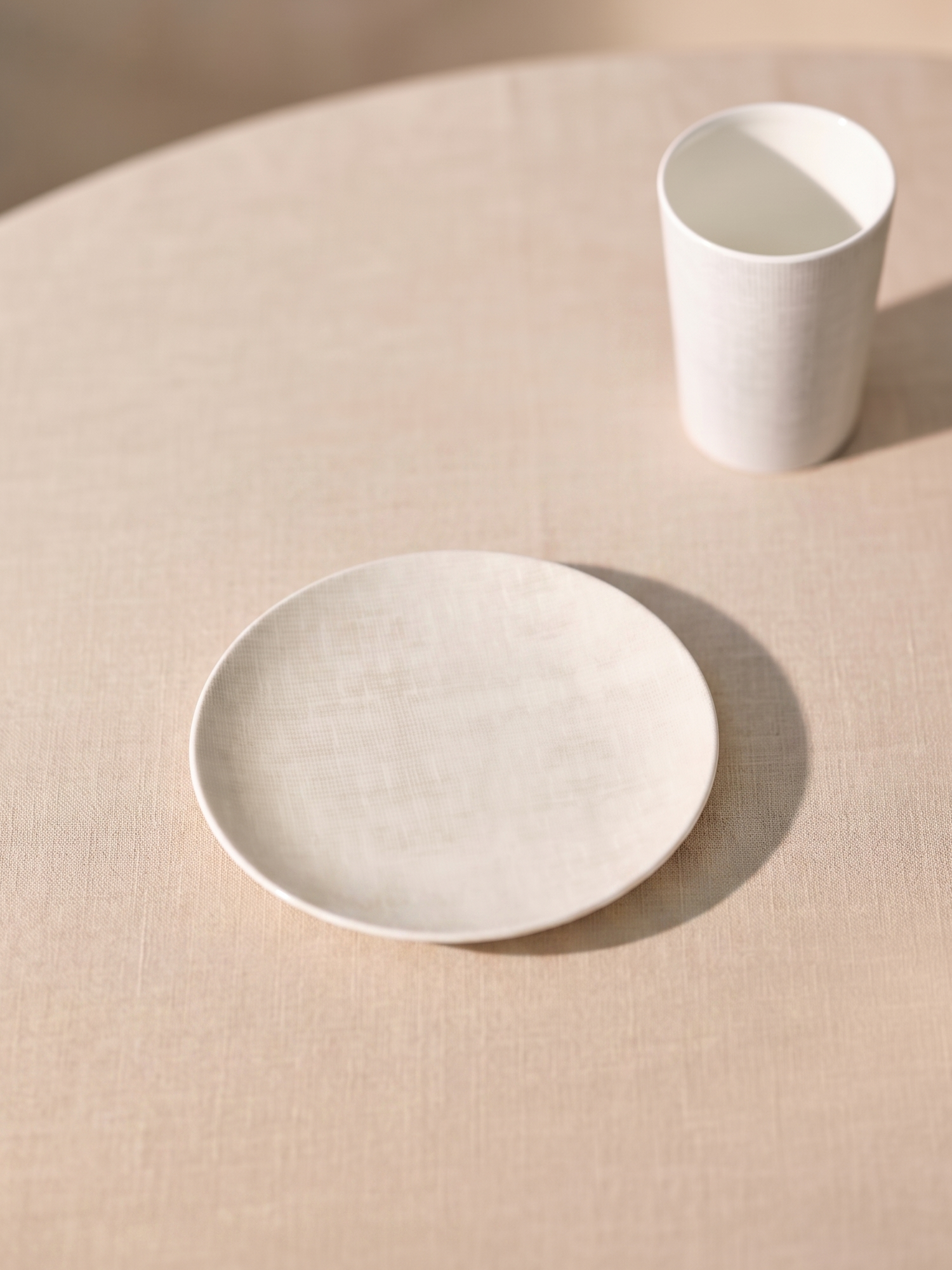 Minimalist white ceramic plate and cup on a beige surface