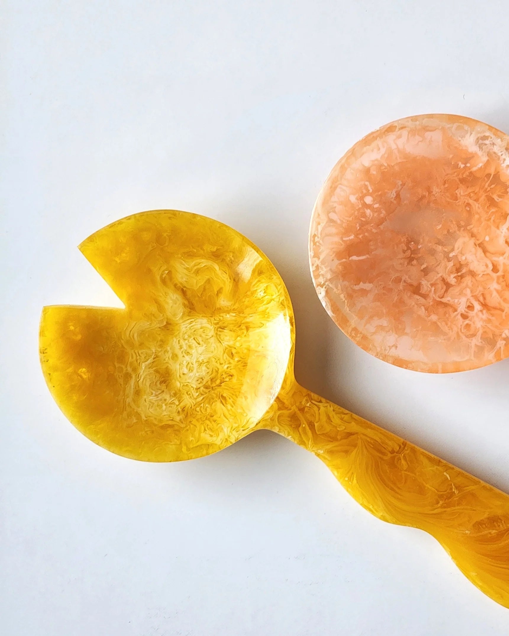 Two decorative spoons, one yellow and one peach-colored, on a white background.