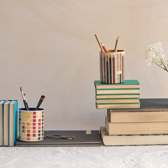 Desk setup with stationery items including books, cups, and a vase.