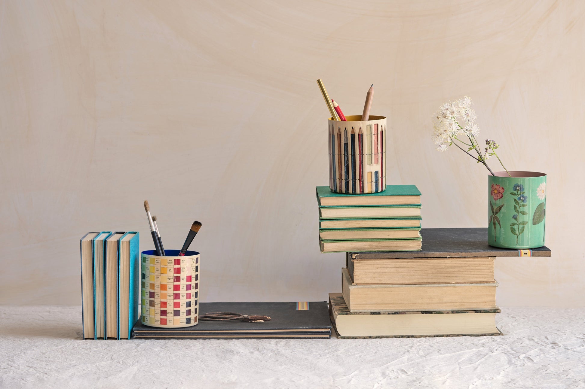 Desk setup with stationery items including books, cups, and a vase.