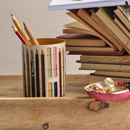 Stack of books with a pencil holder and stationery on a wooden tray against a beige background