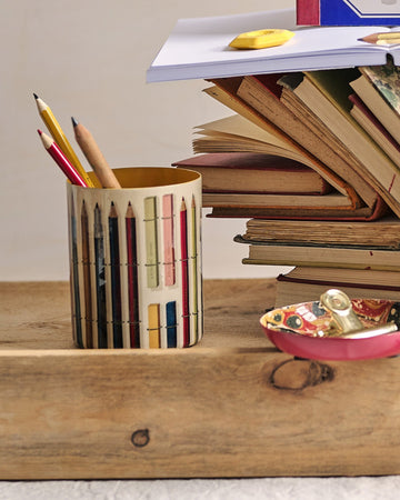 Stack of books with a pencil holder and stationery on a wooden tray against a beige background