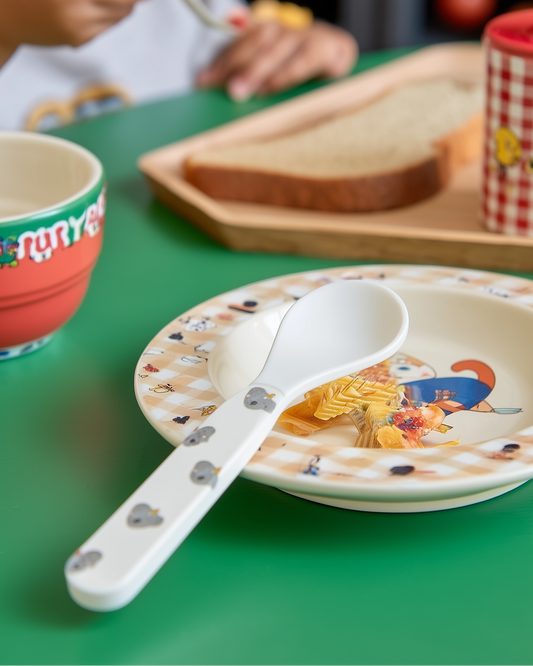 Children's table setting with a plate, bowl, and spoon on a green surface.