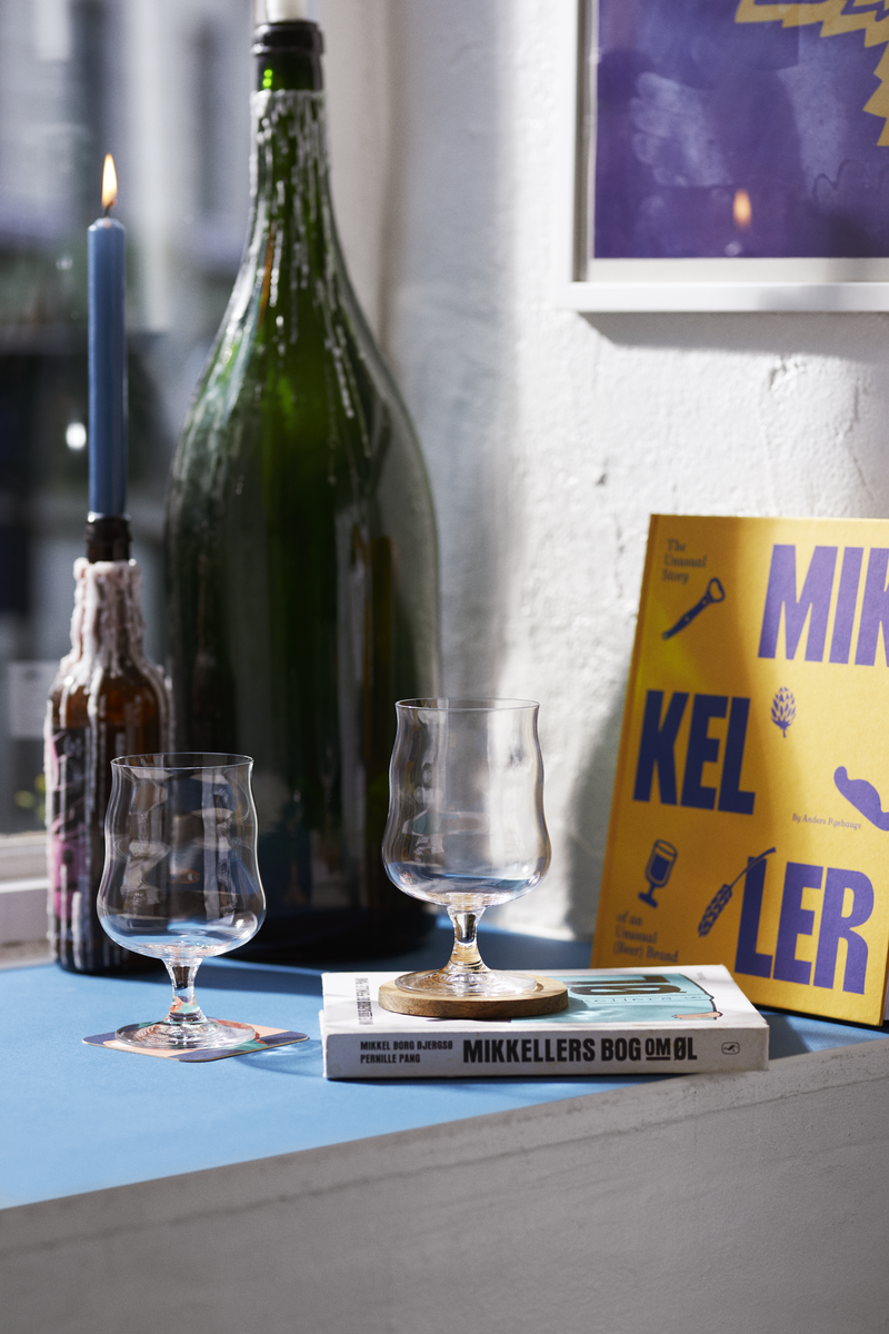 Wine bottle, glasses, and a book titled 'Mikkeller' on a surface with a blurred background.