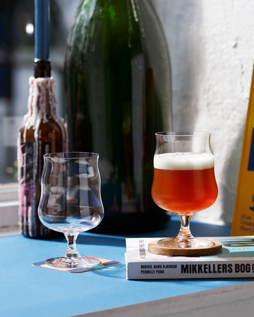 Bottle of beer, glass with beer, and book titled 'Mikkeller' on a surface.
