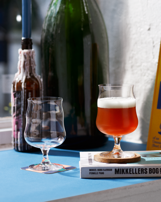 Bottle of beer, glass with beer, and book titled 'Mikkeller' on a surface.