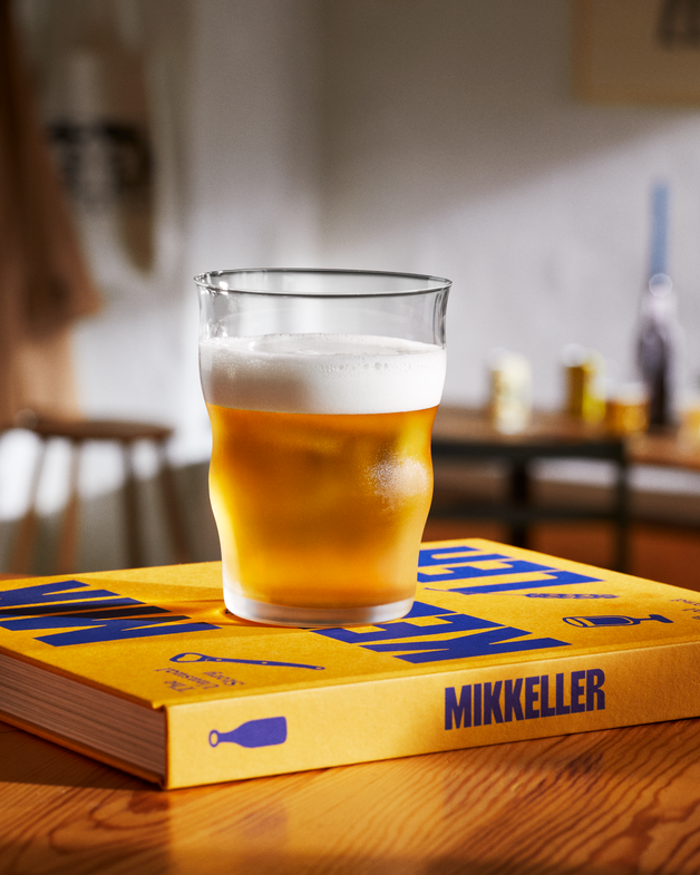 Glass of beer on a Mikkeller branded book on a wooden table