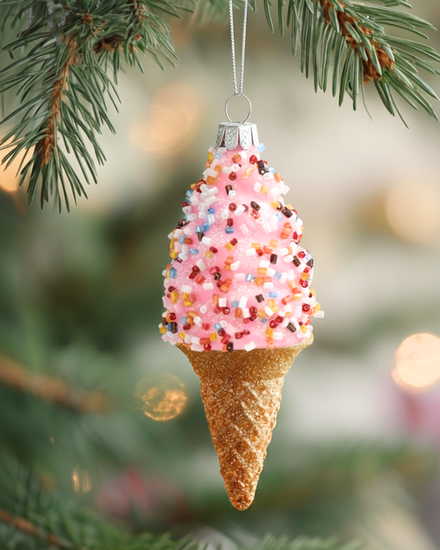 Decorative ice cream cone ornament with pink sprinkles hanging on a Christmas tree.