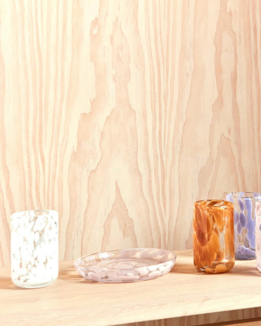 Set of glass mugs and a pitcher on a wooden surface with a light wood panel background